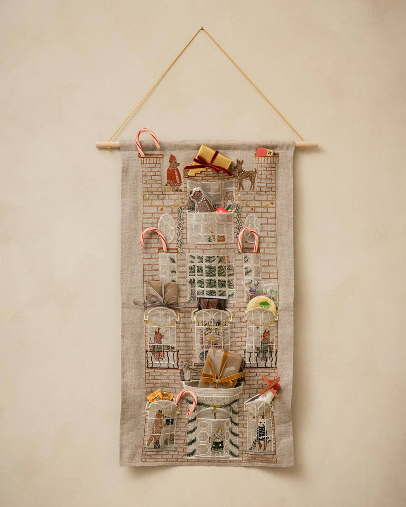 Coral & Tusk Holiday House Advent Calendar wall-hanging with a brick facade illustration and linen pockets filled with small gifts and candy canes.