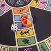A close-up of the 3-in-1 Game Collection: Scrabble, Trivial Pursuit & Cribbage shows the Trivial Pursuit game piece with colorful wedges and a die, evoking classic tabletop fun while highlighting different question categories with icons.