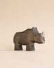 A high-quality Handmade Holzwald Rhino sculpture positioned against a plain, light beige background, showcasing detailed carvings and smooth, dark finish.