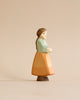 A Handmade Holzwald Goose Girl figurine of a woman with a pastel blue shawl over a peach dress, colored with natural dyes, standing against a plain beige background.