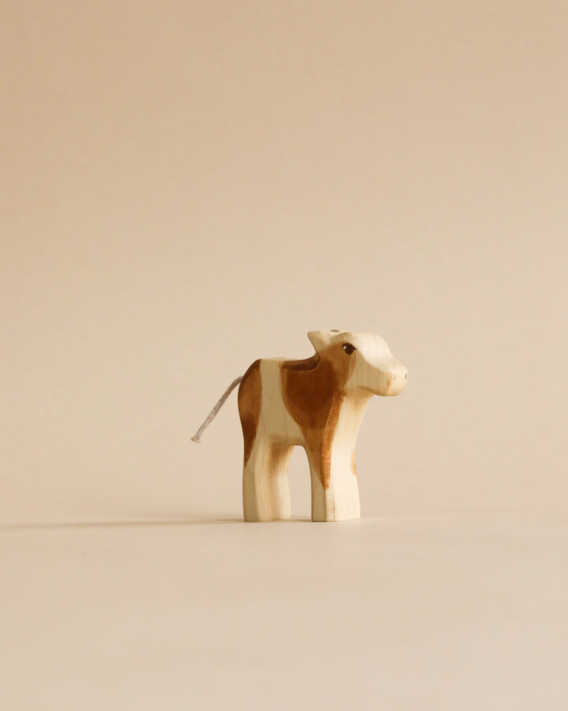 Small Holzwald calf figurine from the Handmade Holzwald Shepherd & Farm Animals Set with brown patches and a cord tail.