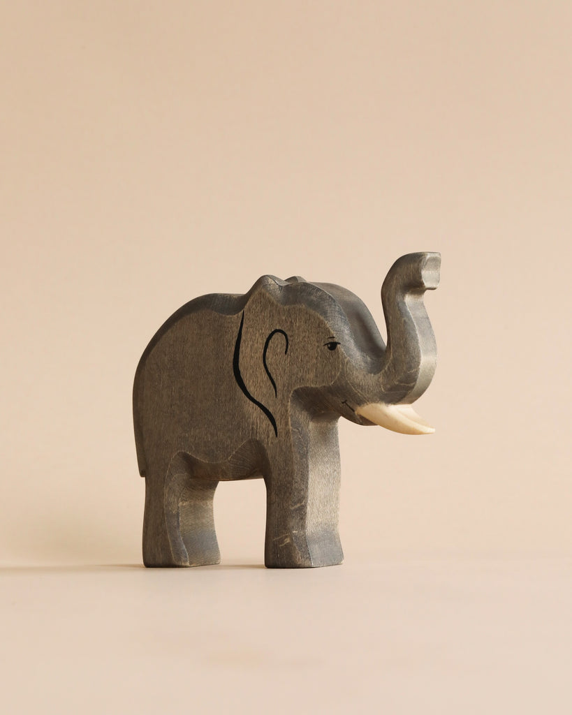 A handmade wooden elephant figurine from the Handmade Holzwald Safari Animals Set with its trunk raised.