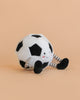 The Mon Ami Sergio Soccer Ball Plush Toy, shaped like a smiling face with striped legs and black shoes, sits on a light beige background—the perfect stuffed soccer toy for any fan.
