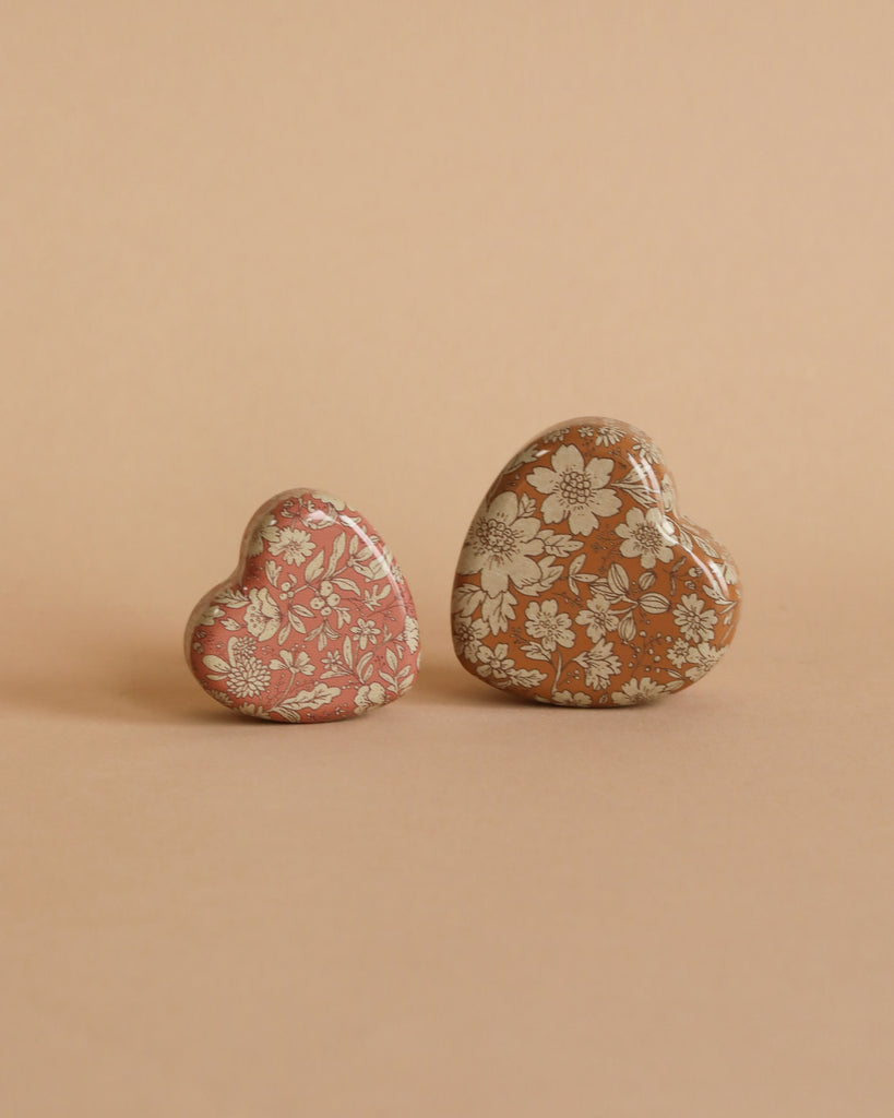 Two heart-shaped objects, including the Maileg Easter Egg with Micro Rabbit & Heart Set—one pink and one brown—are placed side by side on a matching beige background.