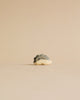 A minimalist image of a small, intricately patterned Handmade Holzwald Hedgehog Baby sculpture with a textured surface, shaped like a star, placed against a light beige background.