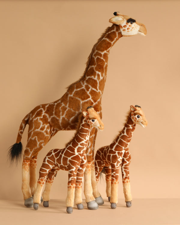 The Safari Giraffe Family Set features three handcrafted plush giraffes in different sizes with realistic brown and cream patterns, standing upright in a group against a plain beige background.