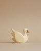 A Handmade Holzwald Swan figurine with a smooth finish and a small black and orange detail on the beak, made from sustainable toys materials, placed against a plain beige background.