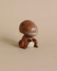 A wooden T-Rex bobblehead shaped like a whimsical creature resembling a mushroom, featuring a rounded cap for a head with a zipper-like smile and small arms and legs, sitting against a plain beige background.
