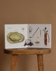Our Big Book of Sports: A Collection of 100+ Sports Words sits open on a wooden stool, showing illustrated golf equipment and a course diagram—ideal for teaching preschool sports vocabulary. Brown background.