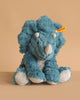 An 11-inch Steiff Dixi Triceratops Dinosaur Plush Toy sits on a beige background, featuring the signature yellow Steiff tag on its left ear that guarantees its authenticity and premium quality.