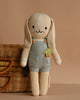 Cuddle + Kind Henry the Bunny is a hand-knit doll with long floppy ears, wearing blue overalls with a carrot detail. Made from 100% cotton yarn for softness and durability, it stands beside a woven basket against a beige background.
