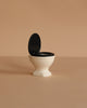 The Maileg Toilet, Mouse Size - Off White features a black seat and lid, shown open against a beige background—an ideal miniature accessory for your SuitCasa mouse house.