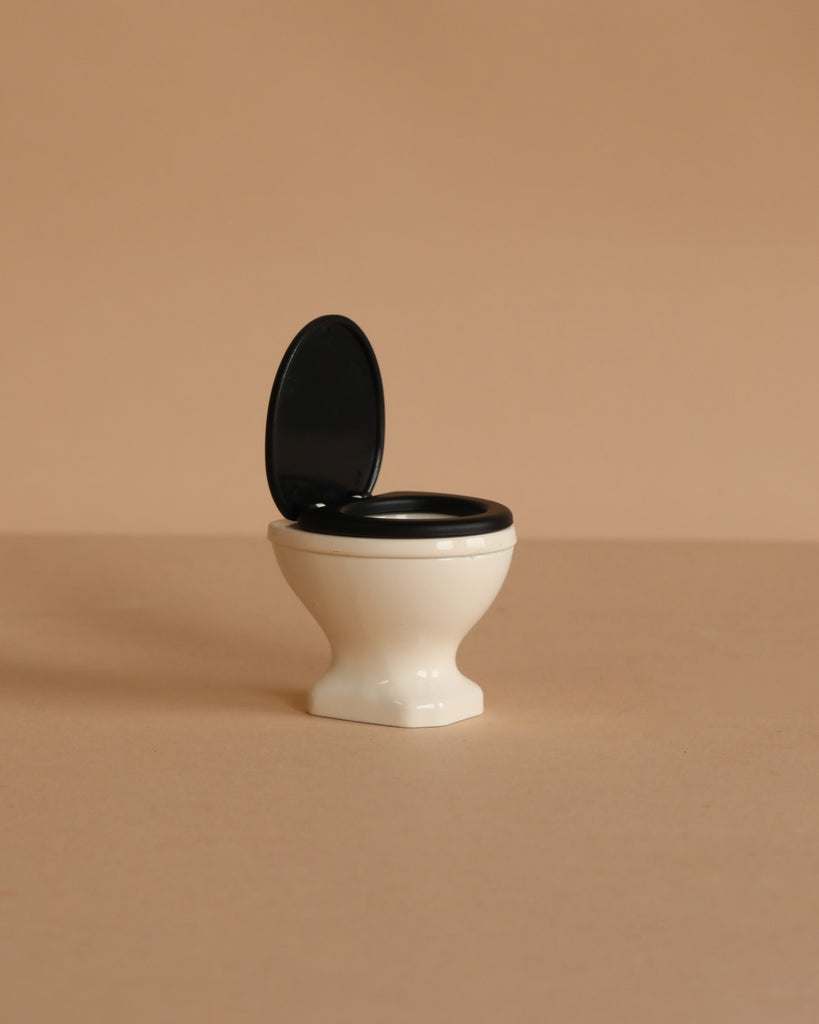 The Maileg Toilet, Mouse Size - Off White features a black seat and lid, shown open against a beige background—an ideal miniature accessory for your SuitCasa mouse house.