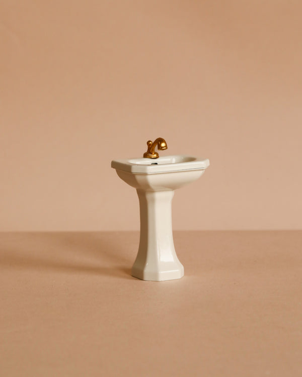 The Maileg Bathroom Sink, Mouse Size - Off White, with a gold faucet, is shown as a charming miniature accessory for a mouse house against a plain beige background.