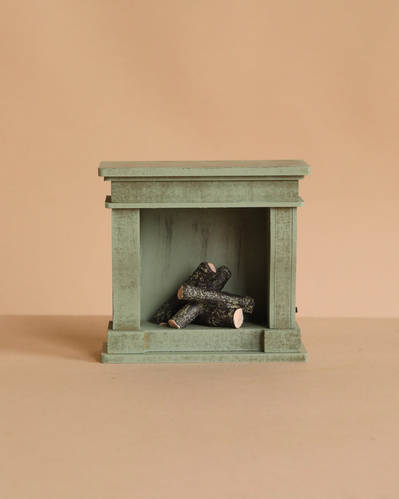 Small sage green Maileg Christmas Room Set miniature fireplace with a stack of wooden logs inside.
