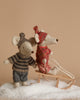 The Maileg Winter Mouse with Ski Set, Big Sister - Rose, features two charming mice adorned in cozy winter attire. One is positioned on a wooden sled crafted from recycled polyester, while the other stands nearby. Both are decked out in knitted hats and sweaters, set against artificial snow with a beige backdrop.