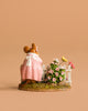 The Wee Forest Folk Tiny Collectible - Annette's Garden features a hand-sculpted mouse in a pink dress beside a white fence with blooming pink flowers and a yellow butterfly, all set against a plain beige background.