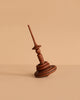 The Mader Apple Helene Top with Spinning Rings, crafted from apple wood, rests at an angle on a beige surface against a matching beige background.