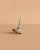 The Mader Spaghetti Spinning Top - Blue, crafted from maple wood with blue and turquoise accents, stands upright on a plain beige surface against a matching background, showcasing its classic charm and safe design.