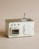 A Maileg Mini Kitchen miniature play kitchen set in neutral tones, featuring a sink, stove, and oven with freshly baked buns inside on a light beige background.