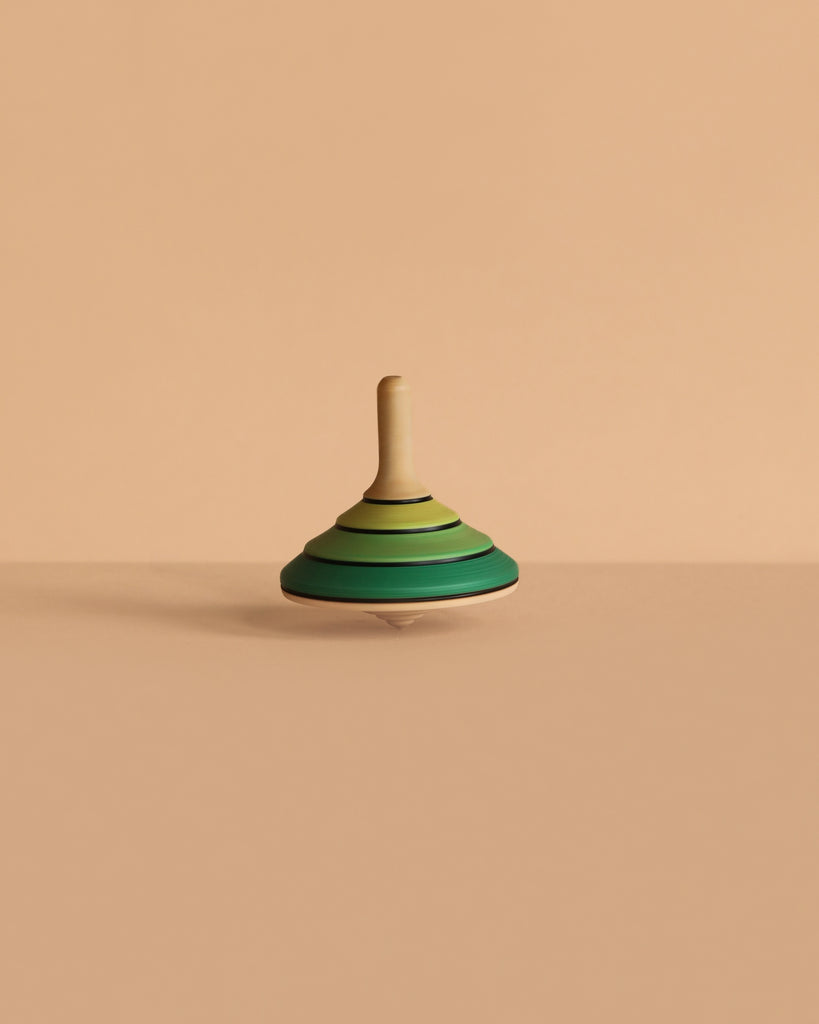 The Mader Tango Spinning Top - Green, made from maple wood, is displayed on a plain beige surface against a matching beige background.