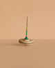 The Mader Spaghetti Spinning Top - Green, featuring a striped handle and crafted from Maple wood, stands upright on a smooth beige surface with a matching plain background.