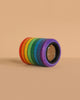 The Mader Rainbow Kaleidoscope, featuring adhesive tape rolls in red, orange, yellow, green, blue, and purple, is stacked on a beige surface and background for a vibrant display reminiscent of a kaleidoscope lens.