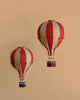 Two burgundy and white striped handmade Hot Air Balloon - Burgundy decorations with wicker baskets float against a beige background. Vintage-inspired, they add whimsical charm to any children's room or space.