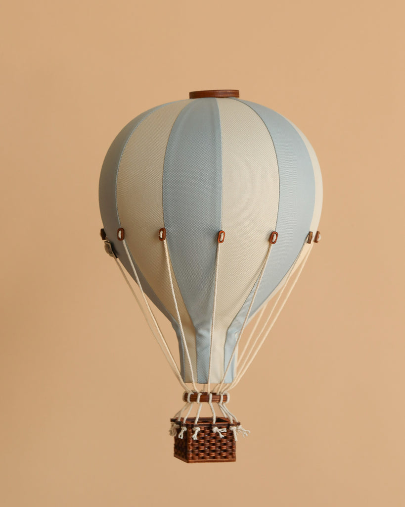 The Hot Air Balloon - Light Blue is a small handmade decor piece featuring alternating light blue and white panels, a brown top, and a basket with white ropes—perfect wooden balloon decor for children's rooms, shown on a beige background.