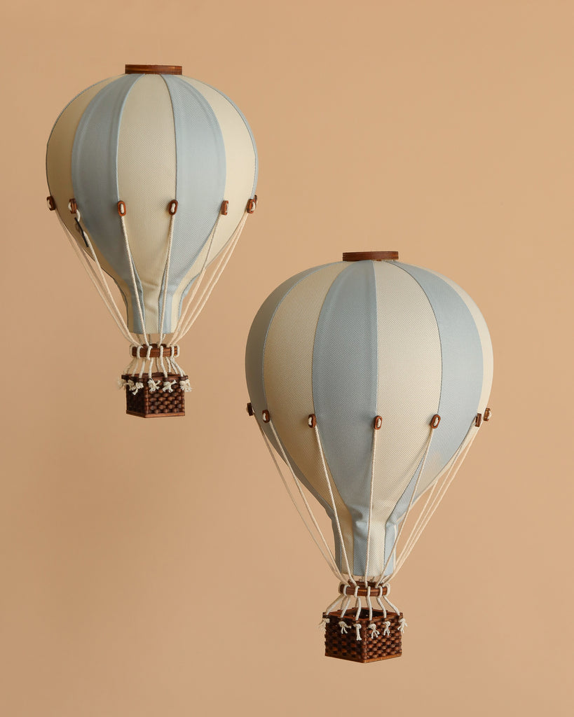 A vintage-style handmade "Hot Air Balloon - Light Blue" with a woven basket floats against a beige background—a charming decorative accent for children's rooms.