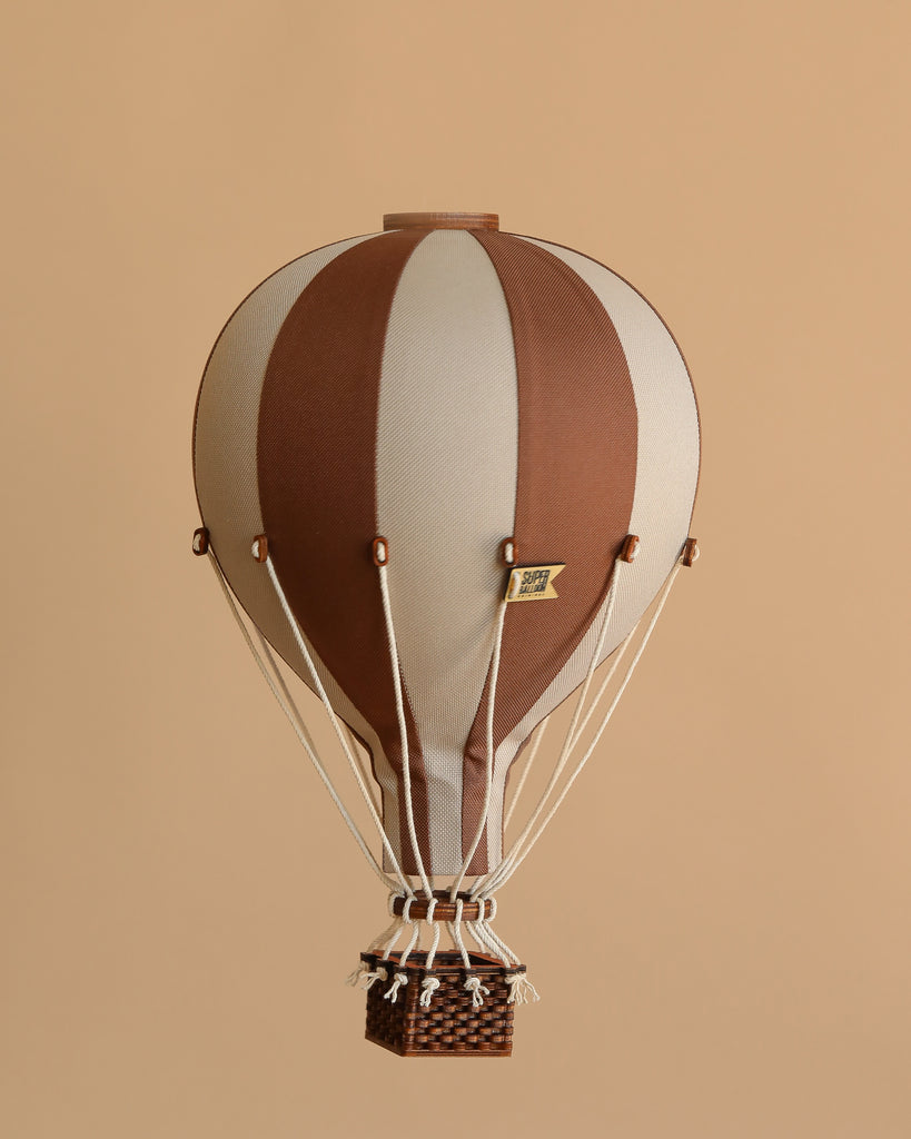 The Hot Air Balloon - Dark Brown features brown and beige stripes with a woven basket, suspended against a plain beige background—ideal as wooden balloon decor for a children's room.