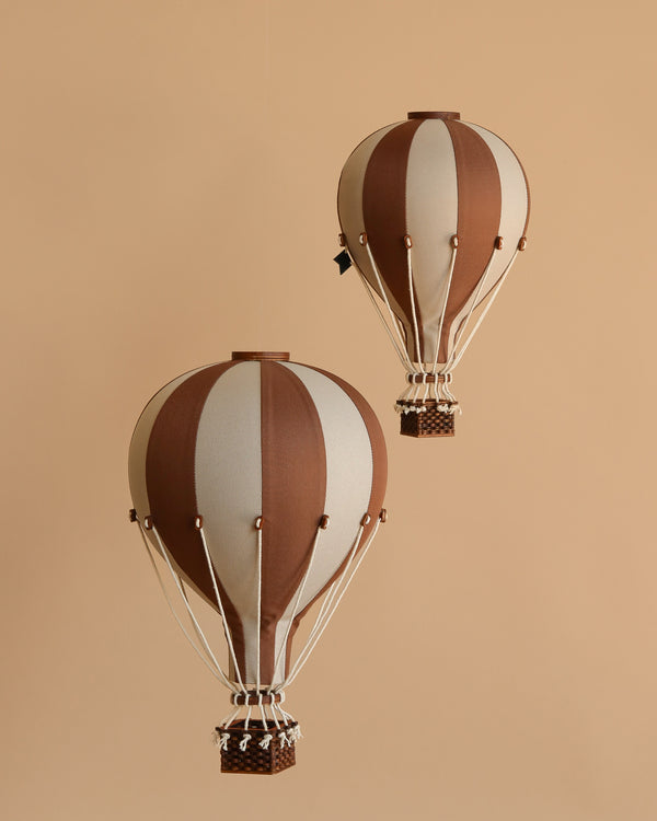 The Hot Air Balloon - Dark Brown features brown and beige stripes with a small basket and decorative ropes, hanging against a beige background—an ideal whimsical touch for decorating a child's room.