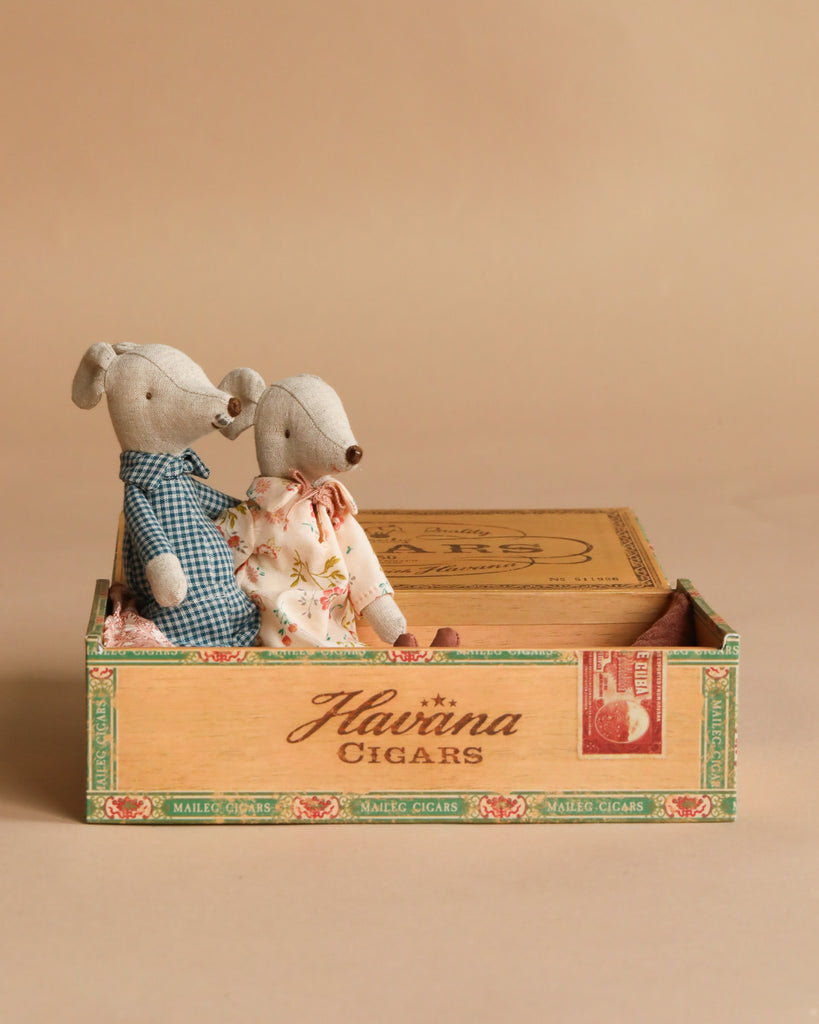 Two Maileg mice dressed as Grandma and Grandpa sit together in a vintage wooden cigar box labeled “Havana Cigars” against a plain beige background, surrounded by charming accessories from the Maileg Kitchen Set.