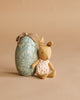 A Maileg Easter Egg & Friends Set features a small Micro Rabbit in a white dress with orange dots beside a blue floral egg with fabric loop, both arranged on a beige background.