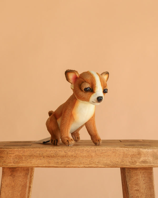 The Chihuahua Tea Cup Dog Stuffed Animal, with brown and white fur, is displayed on a wooden stool against a beige background.