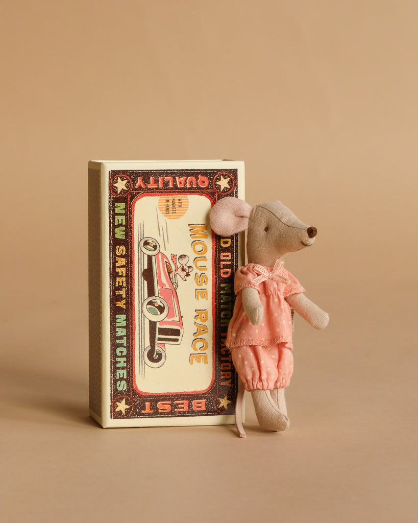 A small Maileg Mouse Family Collection mouse in a pink dress leans against a vintage-style matchbox labeled "Mouse Race" with a car illustration, displayed on a plain beige background.