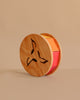 Grimm's Sound and Color Wheel is a wooden baby toy with circular sides featuring geometric cutouts and colorful blocks inside, ideal for motor skills development. Shown here against a plain beige background.
