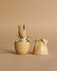 The Maileg Easter Egg with Micro Rabbit, Small - Cream Yellow features a soft rabbit in a blue dress inside a yellow, floral-patterned egg-shaped container with a cream bow lid, set against a beige background.