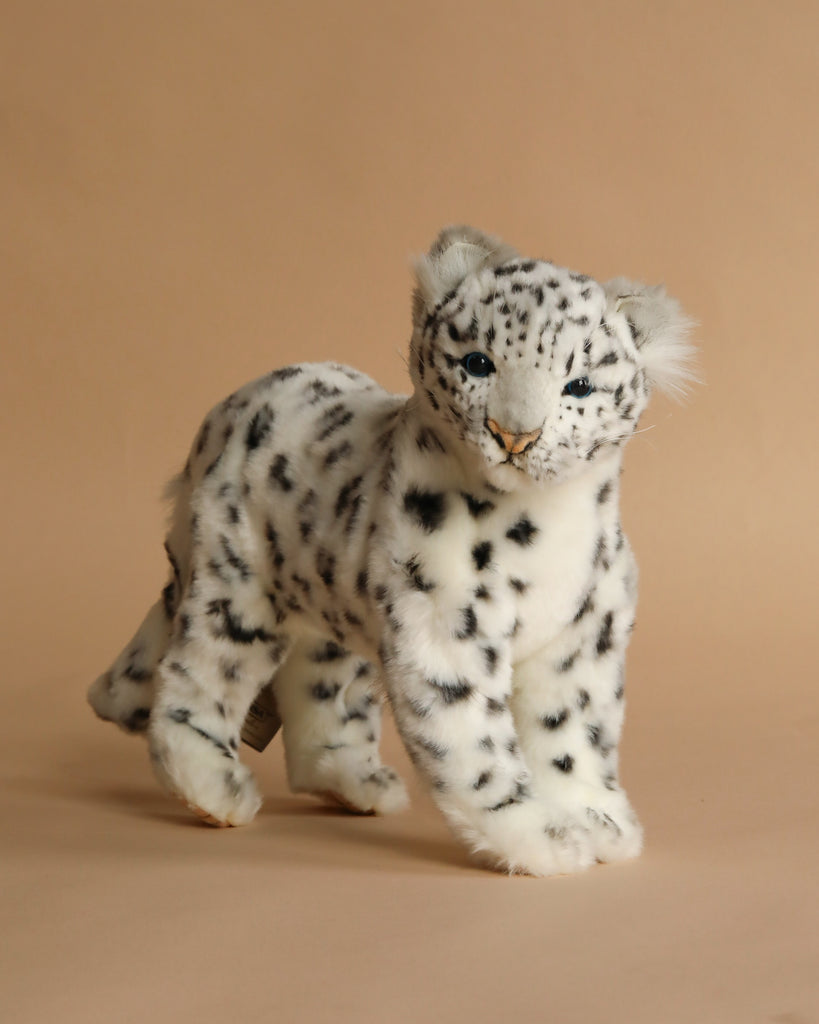 The Snow Leopard Standing Stuffed Animal features soft white fur with black spots, blue eyes, and a realistic look. Perfect for fans of lifelike plush toys, it stands on a light beige background.