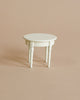A small, white, round Maileg | Mini Side Table with three legs, photographed against a plain beige background. The table has simple, elegant design elements on its legs.