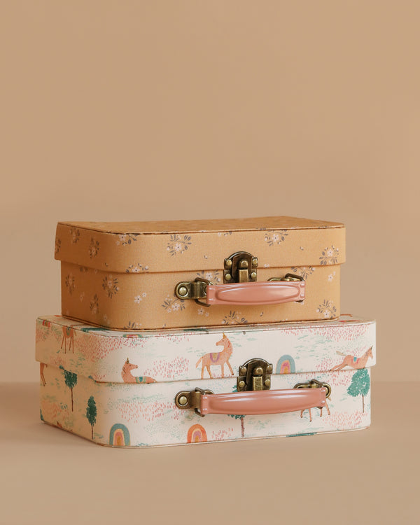 The Maileg Suitcase Set, 2-Pieces - Unicorn features a brown floral suitcase stacked with a white one adorned with playful animal and rainbow designs. Both have metal clasps and pink handles, ideal for charming toy storage.