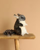 A Chinchilla Stuffed Animal with gray and white fur sits upright on a wooden surface against a plain beige background, highlighting its realistic features.