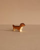 The Handmade Holzwald Dachshund Dog, Small, is a charming brown and white wooden figurine displayed on a beige surface—perfect for lovers of sustainable and classic wooden toys.