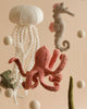 A Handmade Mobile - On The Reef - Final Sale, handmade in Europe, featuring felt sea creatures: a white jellyfish with trailing tentacles, a pink octopus with detailed tentacles, a gray seahorse with a pink fin, and several white felt balls hanging on strings—perfect for visual development and nursery decoration.