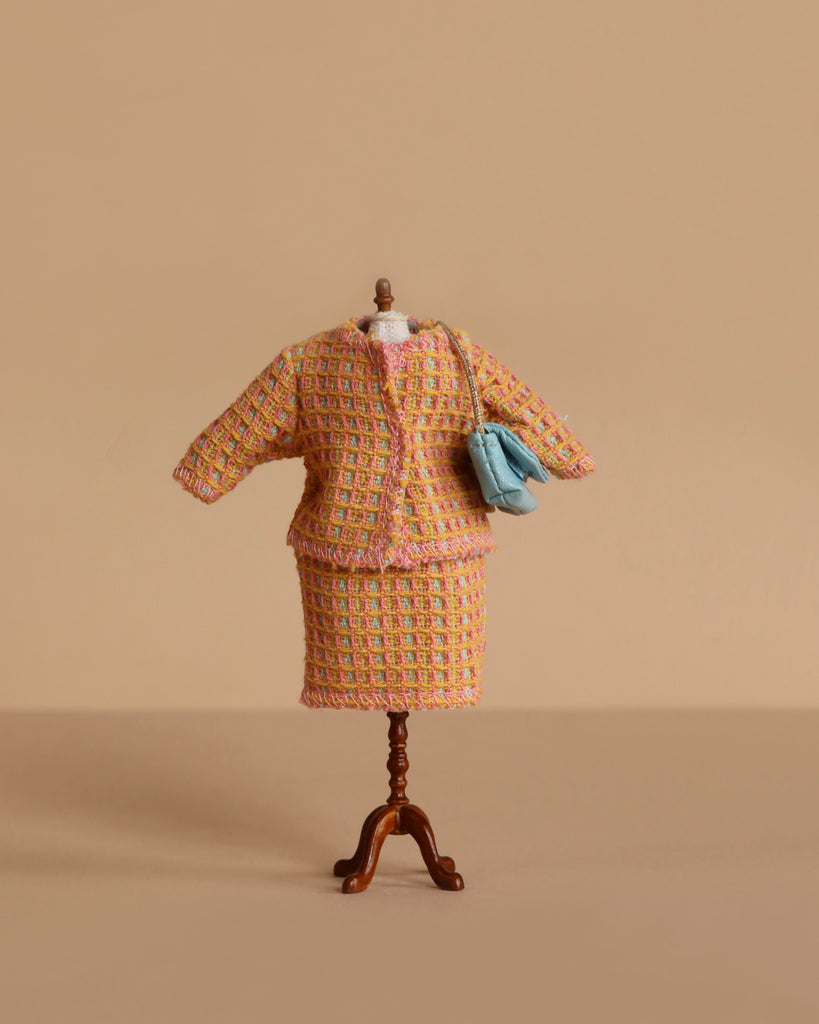 The Maileg Mum Mouse Wardrobe Set, displayed on a miniature mannequin with a pastel tweed outfit and small blue handbag, is perfect for the Maileg Mouse Closet and showcased against a plain beige background.