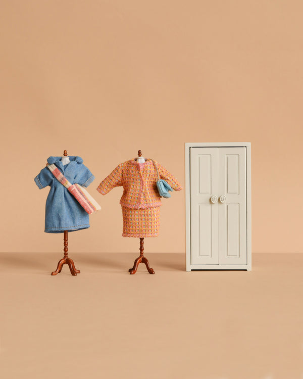 Two miniature dress forms display tiny vintage outfits from the Maileg Mum Mouse Wardrobe Set, standing next to a small white mouse closet against a beige background.