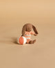 The Maileg Micro Bunny With Ball - Brown - Dusty Rose (Magnetic Hands) sits on a beige surface beside a round orange and white ball, making it a charming storytelling toy.