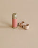 The Maileg Outdoor Tea Set features a pink thermos with gold accents and two small pink cups with black handles, arranged on a beige background—ideal for pairing with Maileg mouse furniture.