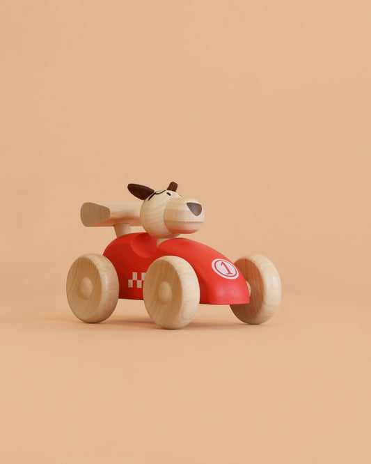 The Wooden Race Car Toy with Dog Driver from Egmont Toys features a vibrant red body, natural wood wheels, and a playful dog figure behind the wheel. Set against a plain beige background, this charming toy showcases classic red sports car appeal paired with timeless wooden craftsmanship.