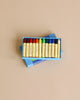 The Stockmar Crayon Set features a non-toxic, vibrant 10-color collection, including yellow, orange, red, purple, green, blue, and black. The crayons are neatly arranged in a wooden organizer tray on a brown surface to meet any artistic demands.